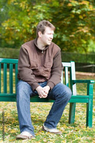 young man in the autumn park sitting on bench