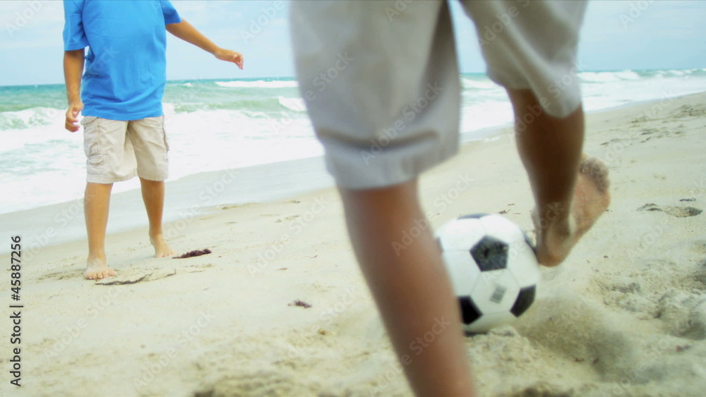 Ethnic brothers kicking together football on beach Ethnic brothers kicking together football on beach