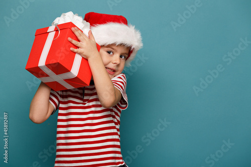 Funny child in Santa red hat holding Christmas gift in hand.
