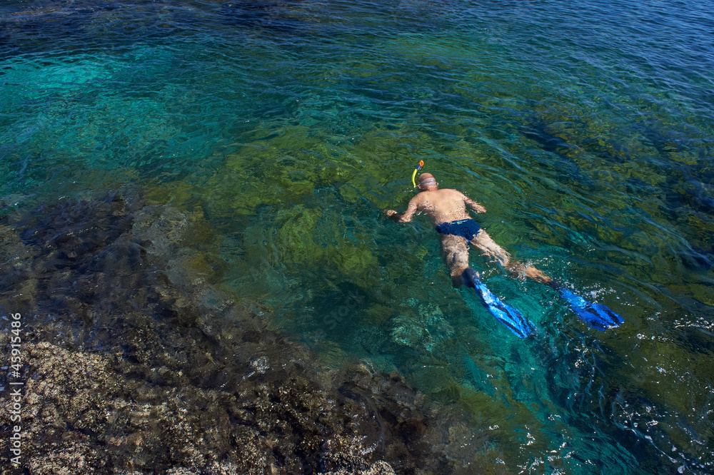 Young man snorkeling in transparent shallow ocean