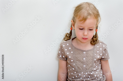 Obraz na plátně Portrait of sad little girl standing against the wall.