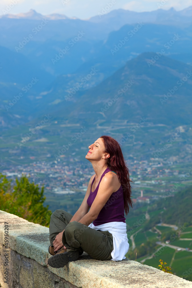 Woman with eyes closed sitting on a ledge.