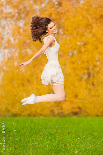 Beautiful young girl in white dress jumping on the background of