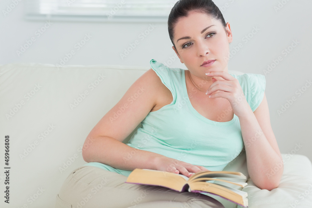 Thoughtful woman reading a book on the couch Thoughtful woman reading a book on the couch