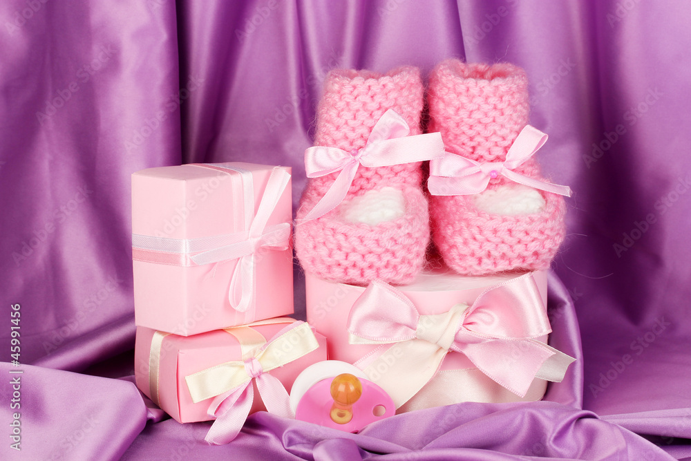 pink baby boots, pacifier, gifts on silk background. pink baby boots, pacifier, gifts on silk background.