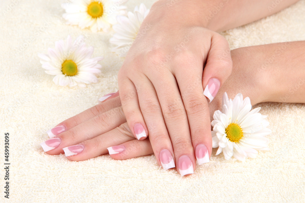 Woman hands with french manicure and flowers on towel Woman hands with french manicure and flowers on towel