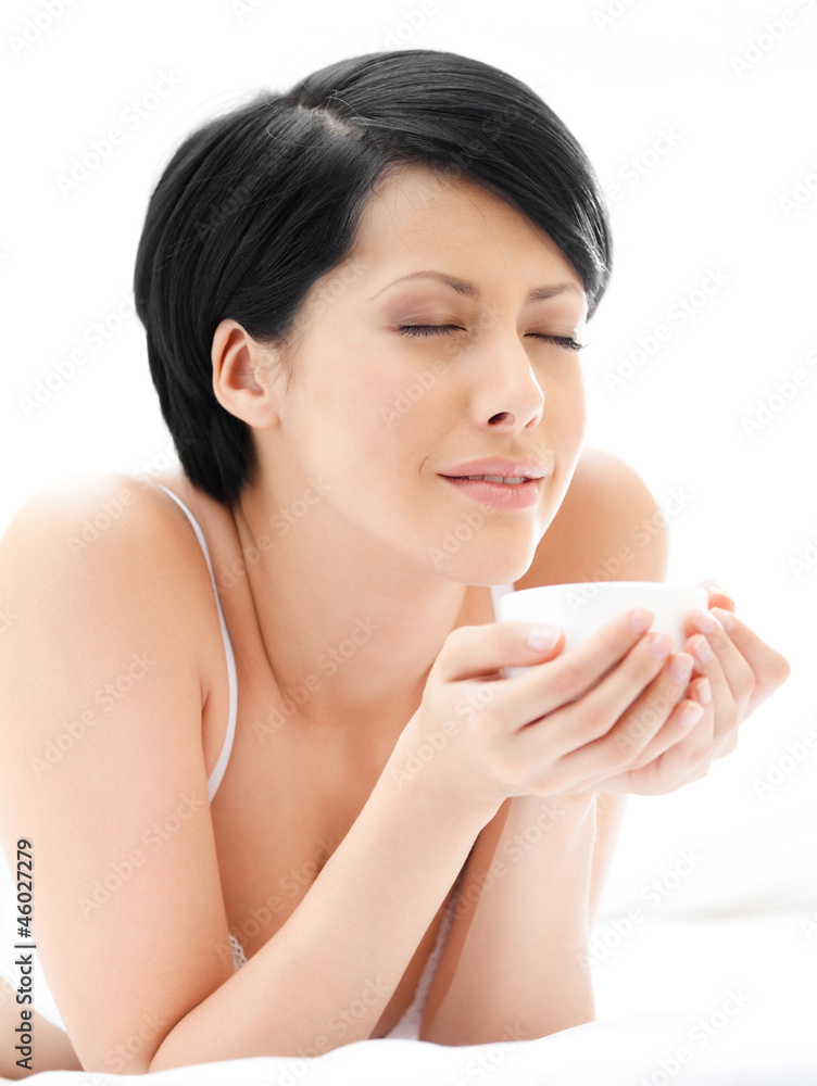 Woman in underwear is lying in the bed with cup of tea Woman in underwear is lying in the bed with cup of tea