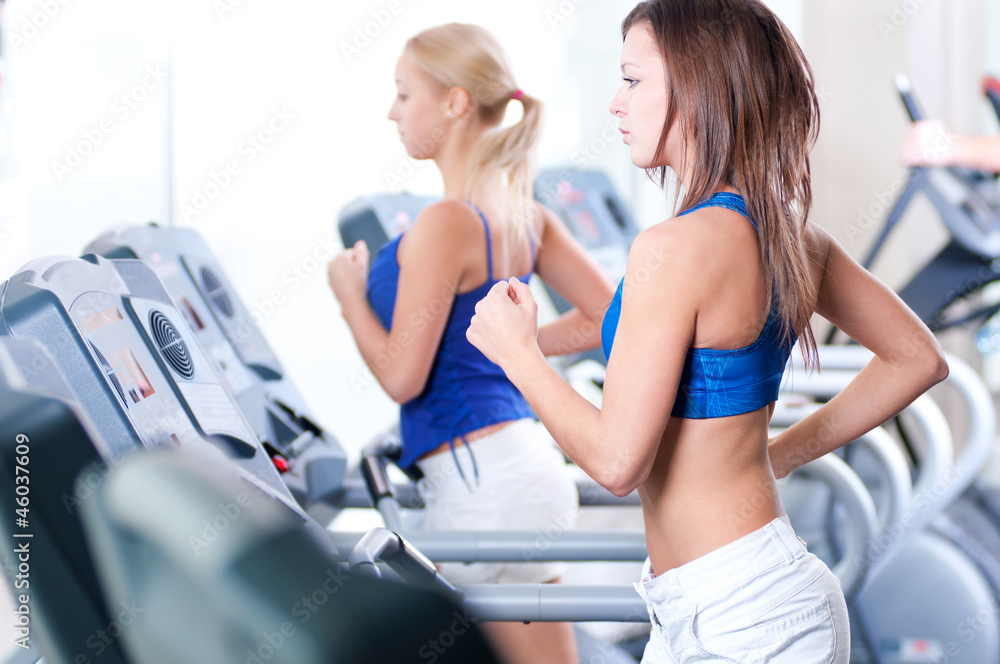 Two young women run on machine in the gym Two young women run on machine in the gym