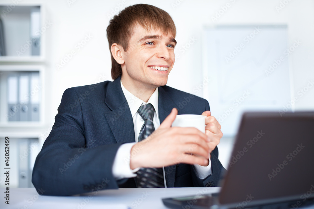 Happy young businessman with cup of coffee in office Happy young businessman with cup of coffee in office