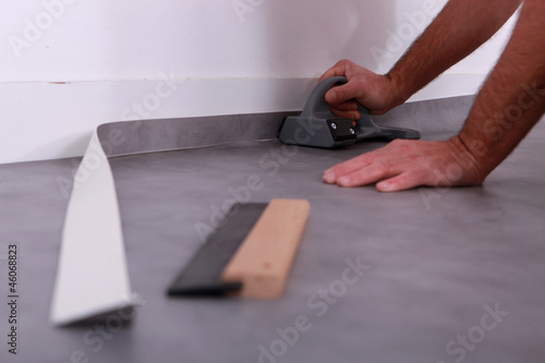Man trimming linoleum against a skirting board