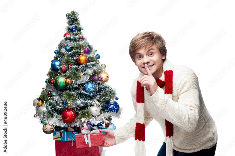 young smiling man puts gift under christmas tree young smiling man puts gift under christmas tree