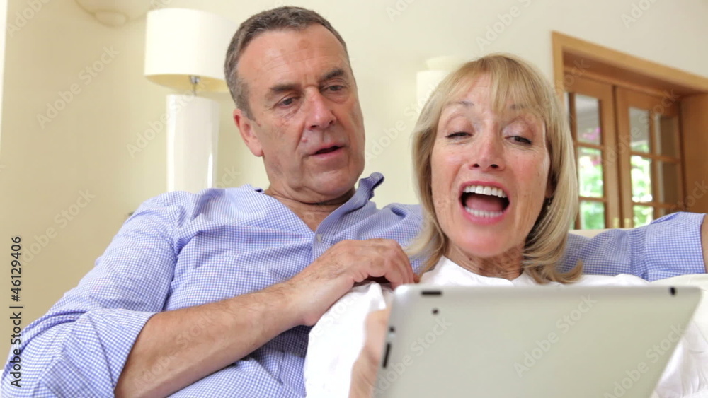 Senior Couple Sitting On Sofa Using Digital Tablet