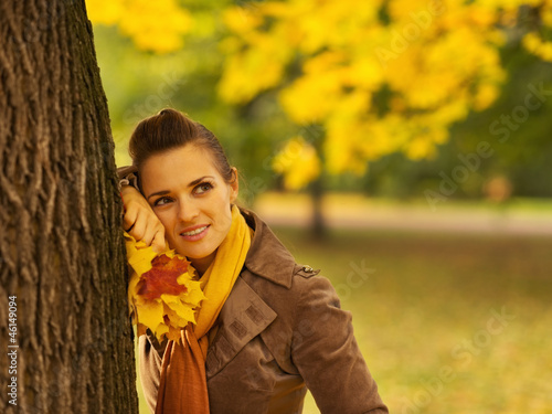 Thoughtful woman with fallen leaves leaning against tree