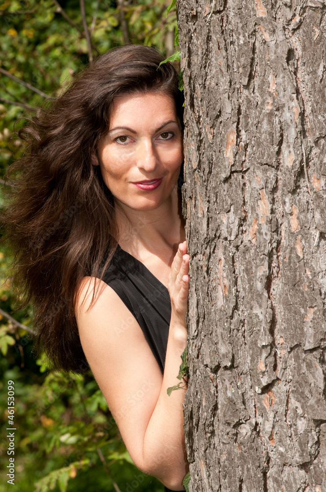 Frau mit langem Haar schaut hinter Baum vor Frau mit langem Haar schaut hinter Baum vor
