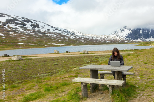 Young girl working on a laptop among mountains