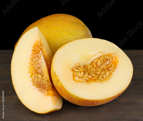 Cut ripe melons on wooden table on black background photo