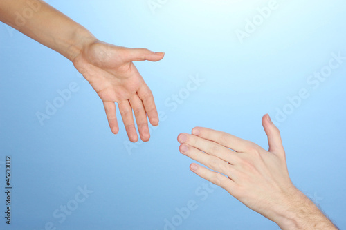 Women's hand goes to the man's hand on blue background © Africa Studio