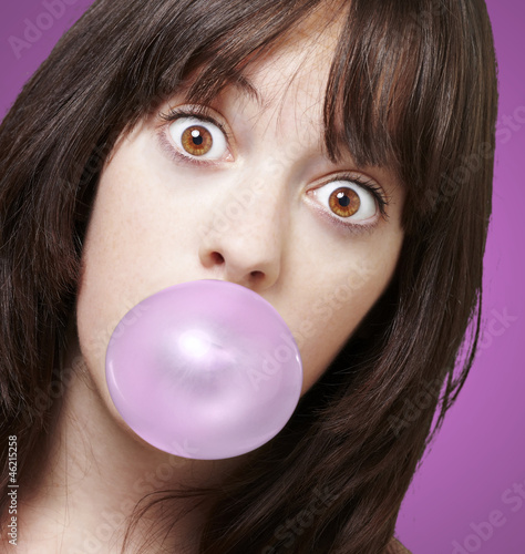 young girl with a pink bubble of chewing gum against a pink back