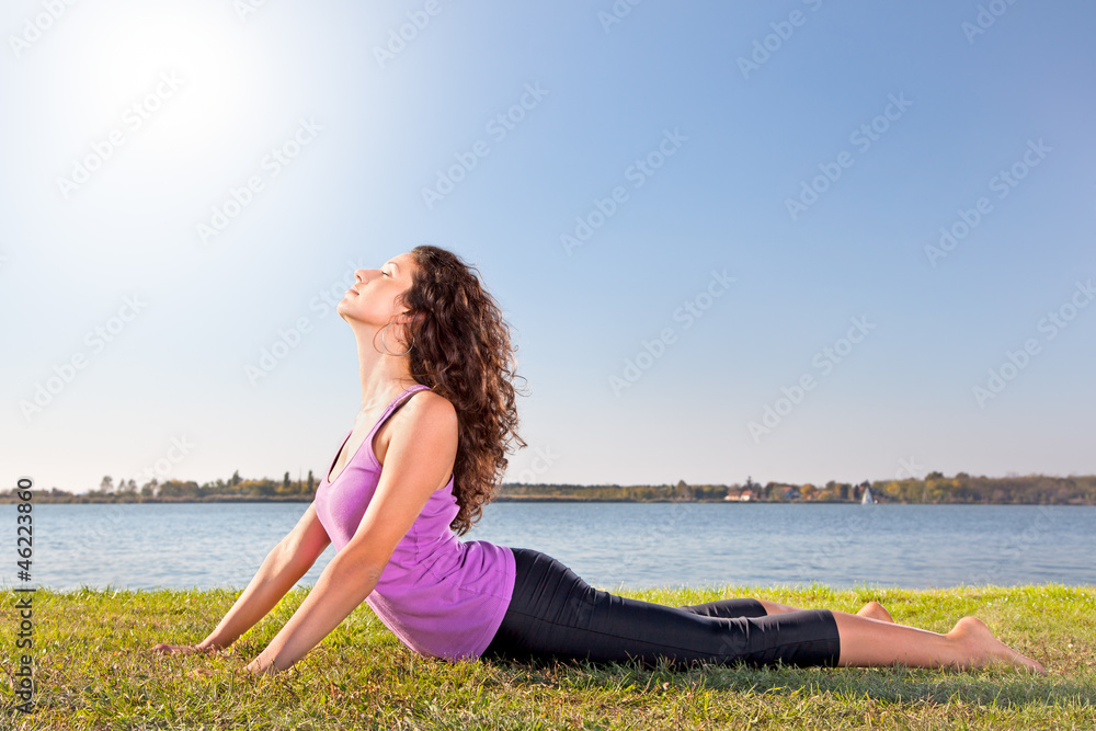 Beautiful young woman doing stretching exercise on green grass.