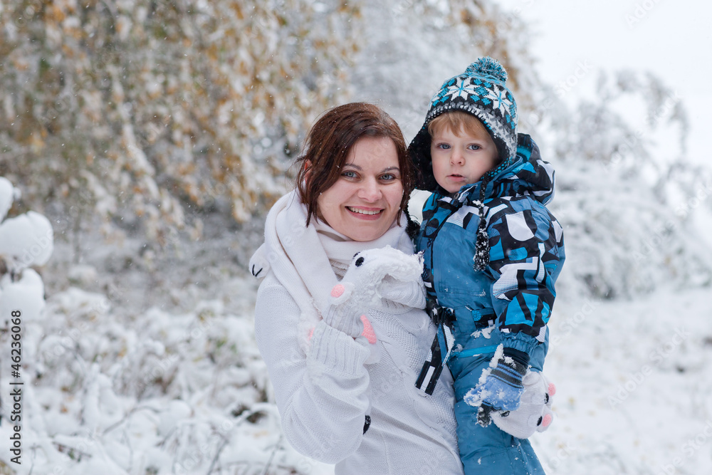 Mother and toddler boy having fun with snow on winter day