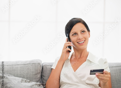 Happy young woman with credit card and speaking mobile phone