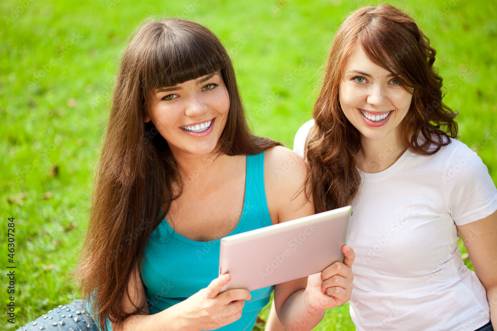 Fototapeta premium Two women in the park on a picnic with a Tablet PC