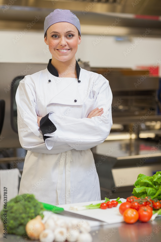 Smiling chef folding her arms beside vegetables Smiling chef folding her arms beside vegetables