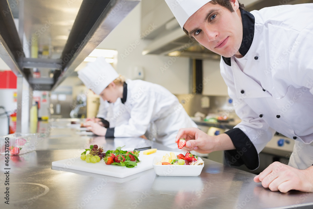 Man chef putting a strawberry in fruit salad Man chef putting a strawberry in fruit salad
