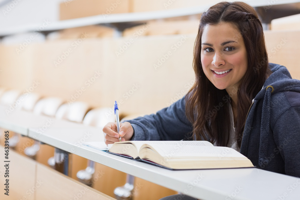 Girl sitting smiling while reading a book and taking notes Girl sitting smiling while reading a book and taking notes