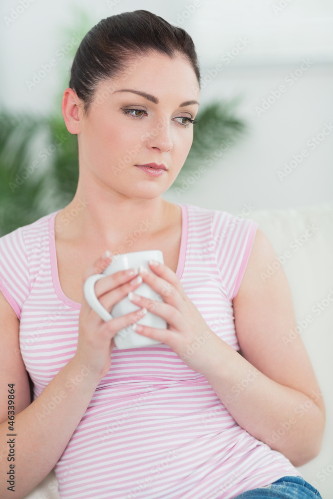 Thoughtfully woman sitting on the couch holding a mug Thoughtfully woman sitting on the couch holding a mug