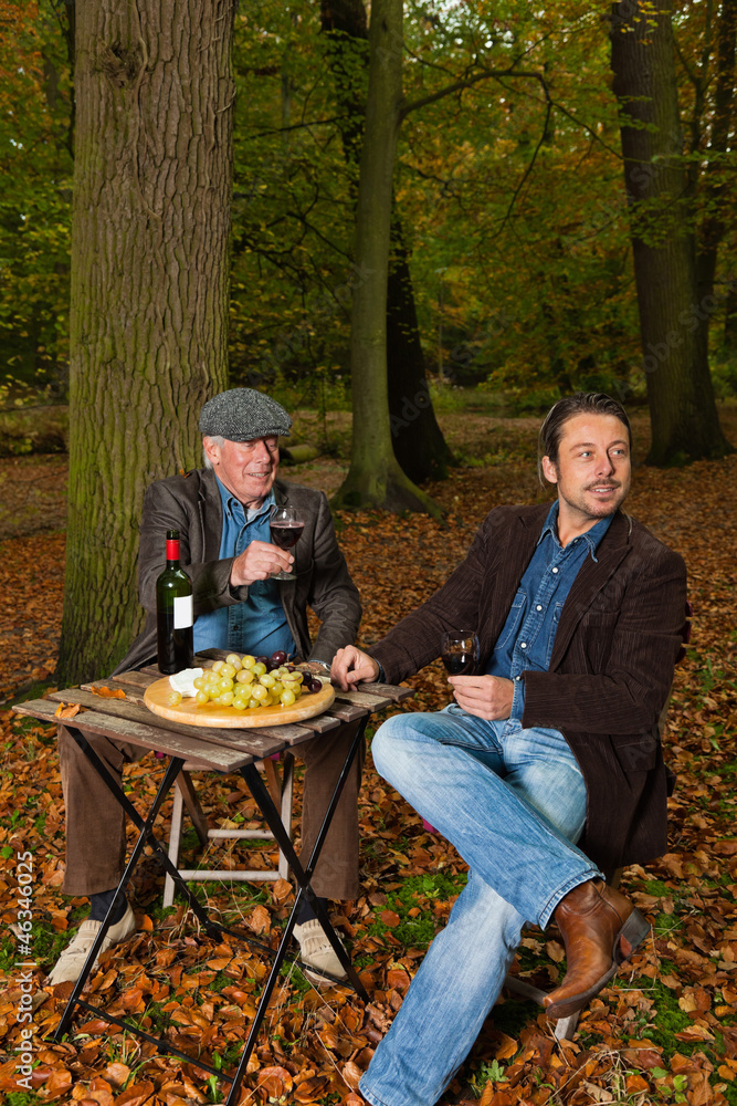 Senior and young man enjoying red wine in autumn forest. Senior and young man enjoying red wine in autumn forest.