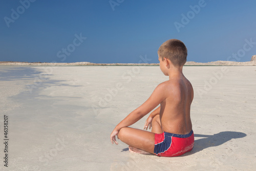 The little boy meditating on the beach