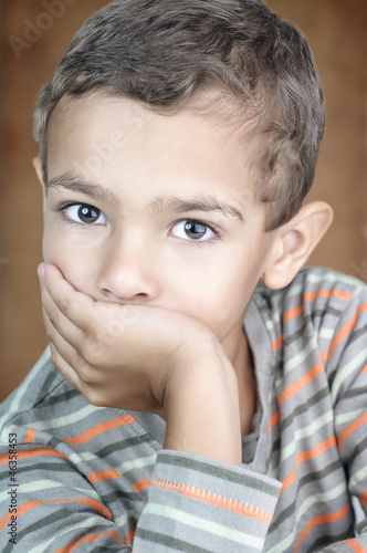 Portrait of cute litle boy covering his mouth