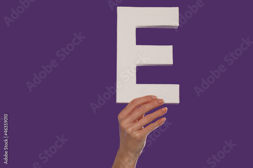 Female hand holding up the letter E from the bottom