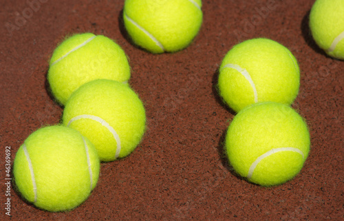 Seven Yellow tennis balls lays on brown court closeup