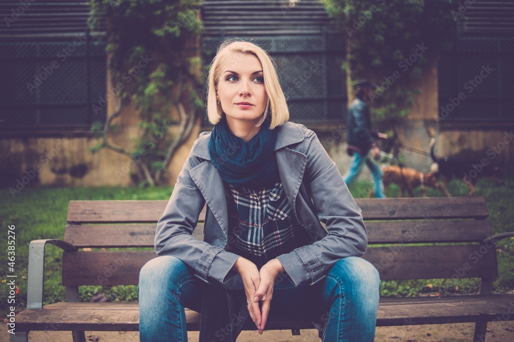 Beautiful pensive blond woman sitting on bench in park outdoors Beautiful pensive blond woman sitting on bench in park outdoors