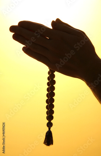 male hands with rosary, on yellow background