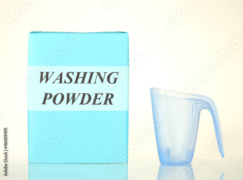 Box of washing powder with blue measuring cup isolated on white