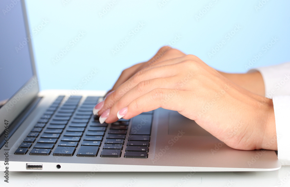 Hands typing on laptop keyboard close up on blue background Hands typing on laptop keyboard close up on blue background