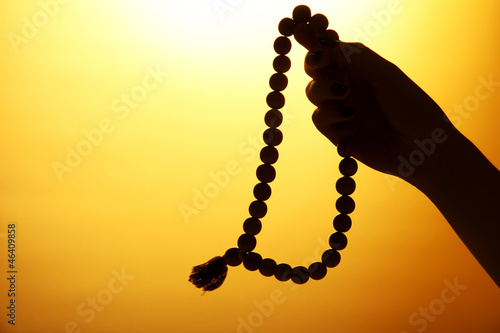 female hands with rosary, on yellow background
