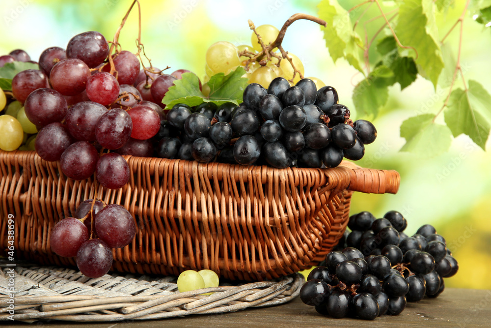 assortment of ripe sweet grapes in basket, on green background assortment of ripe sweet grapes in basket, on green background