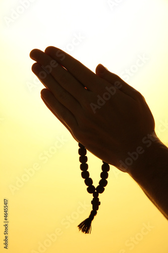 male hands with rosary, on yellow background