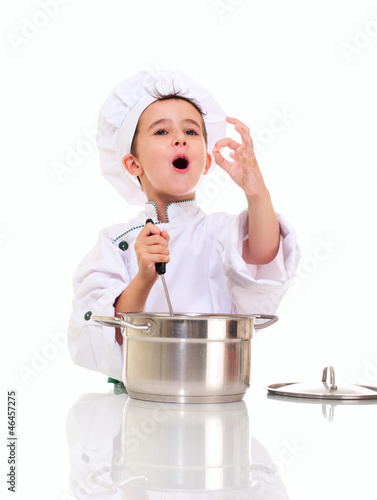 Little singing boy chef in uniform with ladle stiring in the pot