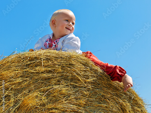 Little boy sits on the big hay bale roll