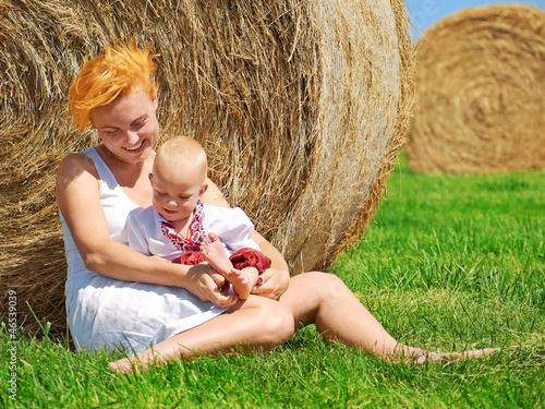 Young woman and little son on the field with big hay bale rolls