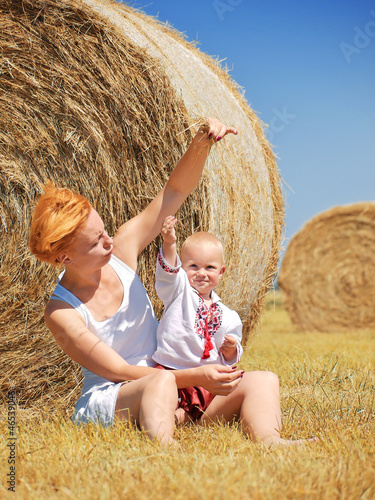 Young woman and little son on the field with big hay bale rolls