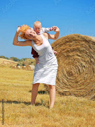 Young woman and little son on the field with big hay bale rolls