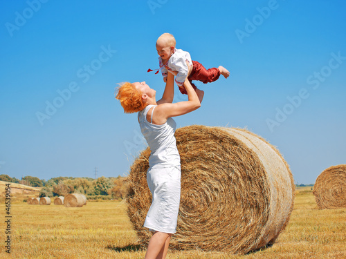 Young woman and little son on the field with big hay bale rolls