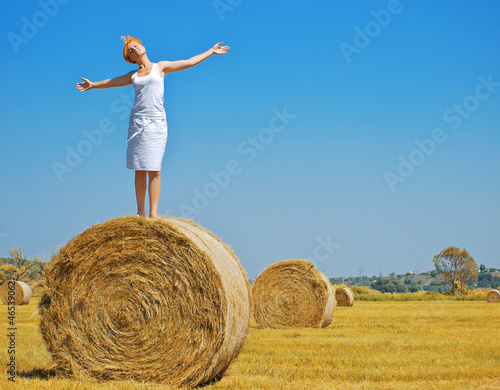 Young woman having fun on the field with big hay bale rolls