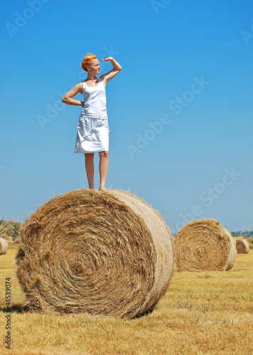 Young woman having fun on the field with big hay bale rolls